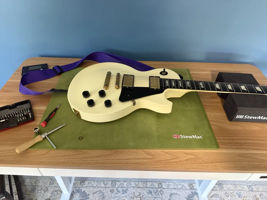 Cream 1990s Gibson Les Paul Studio with gold hardware on a StewMac bench mat, with the jack tool and a bit set beside it
