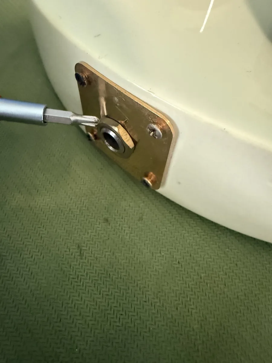 Screwdriver pointing at the loose output jack nut on the gold jack plate of a cream Les Paul