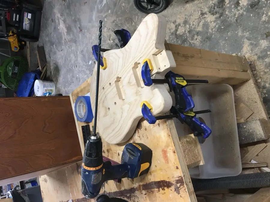 Drilling a clamped guitar body with a cordless drill at the workbench