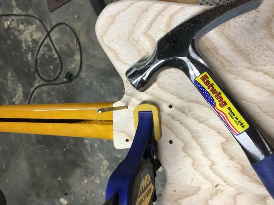 Hammer, clamps and drill bit set up over a guitar body blank