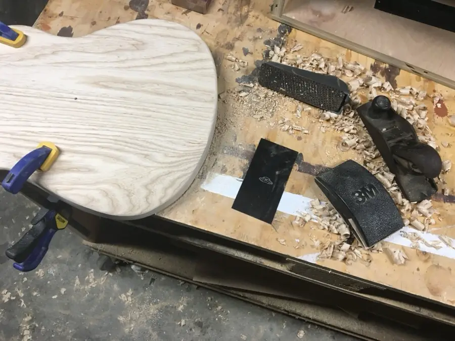 Chisels and rasps on the bench beside a body and fresh shavings