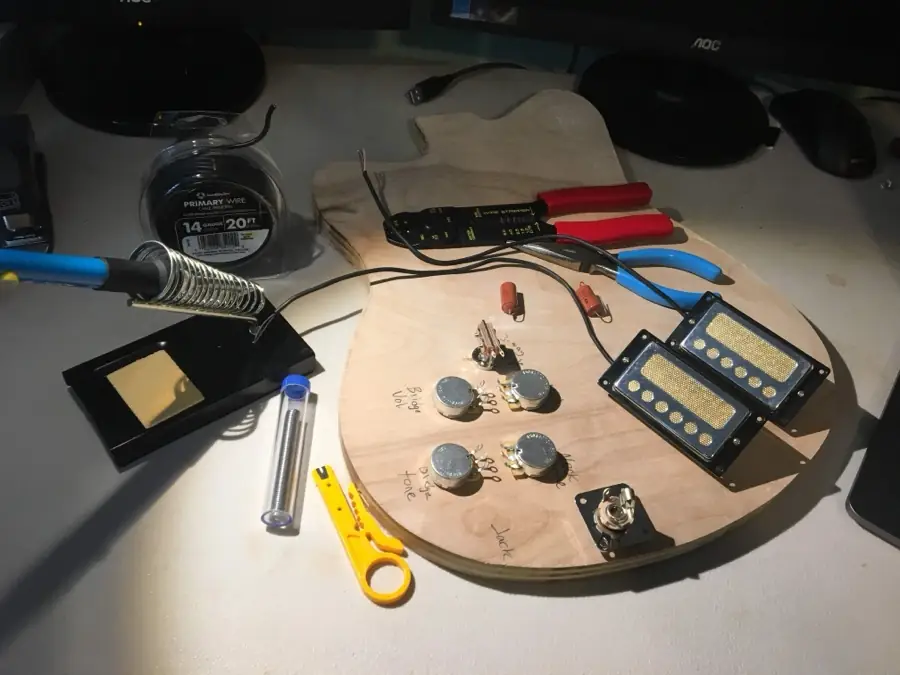 Soldering iron, wire spool, strippers, pots and pickups laid out on a body blank